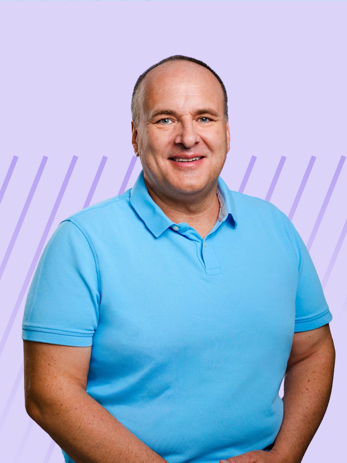 Bald man in a light blue polo shirt smiling against a purple background.