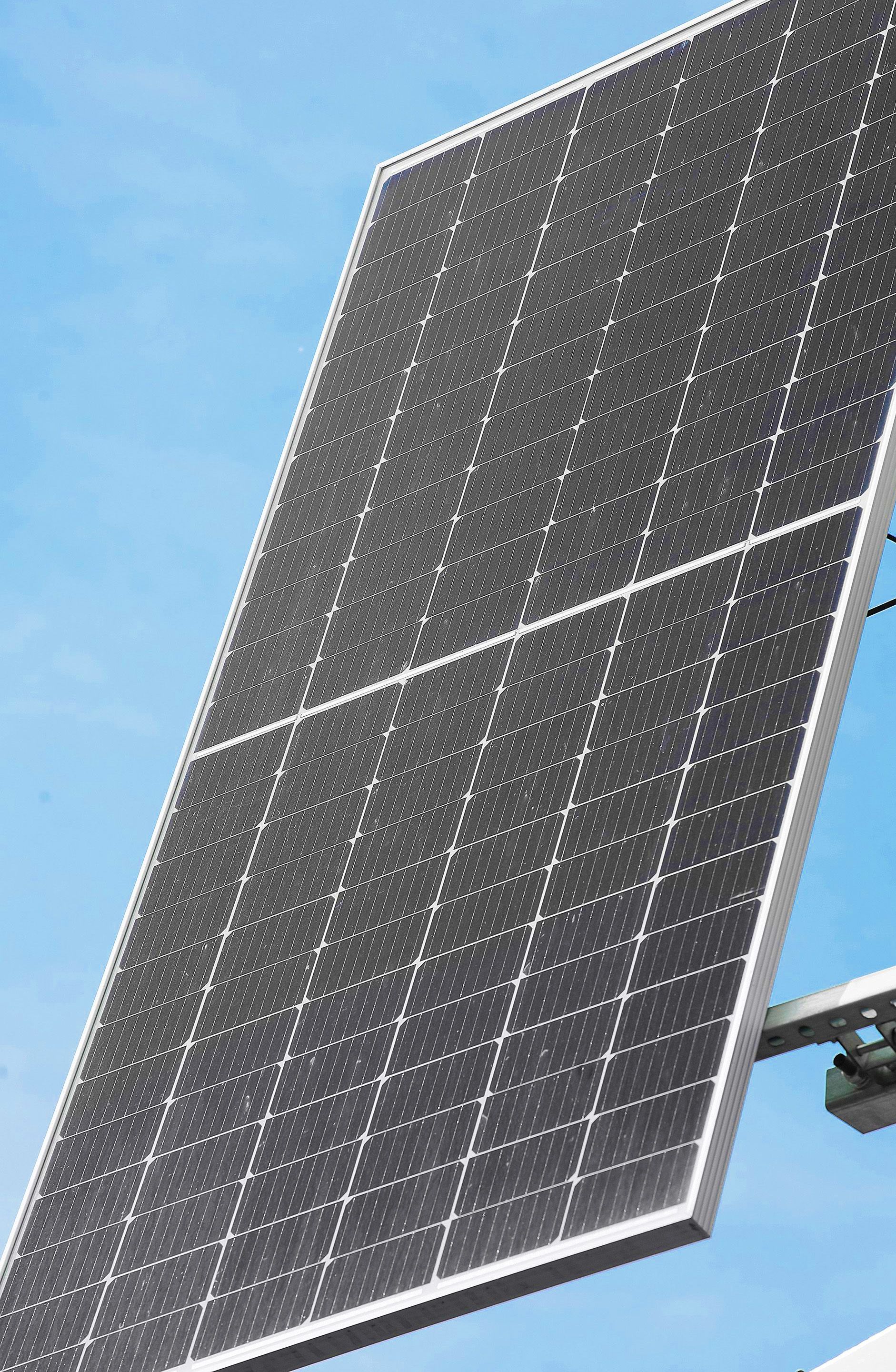 A close-up of a solar panel angled upwards against a clear blue sky.