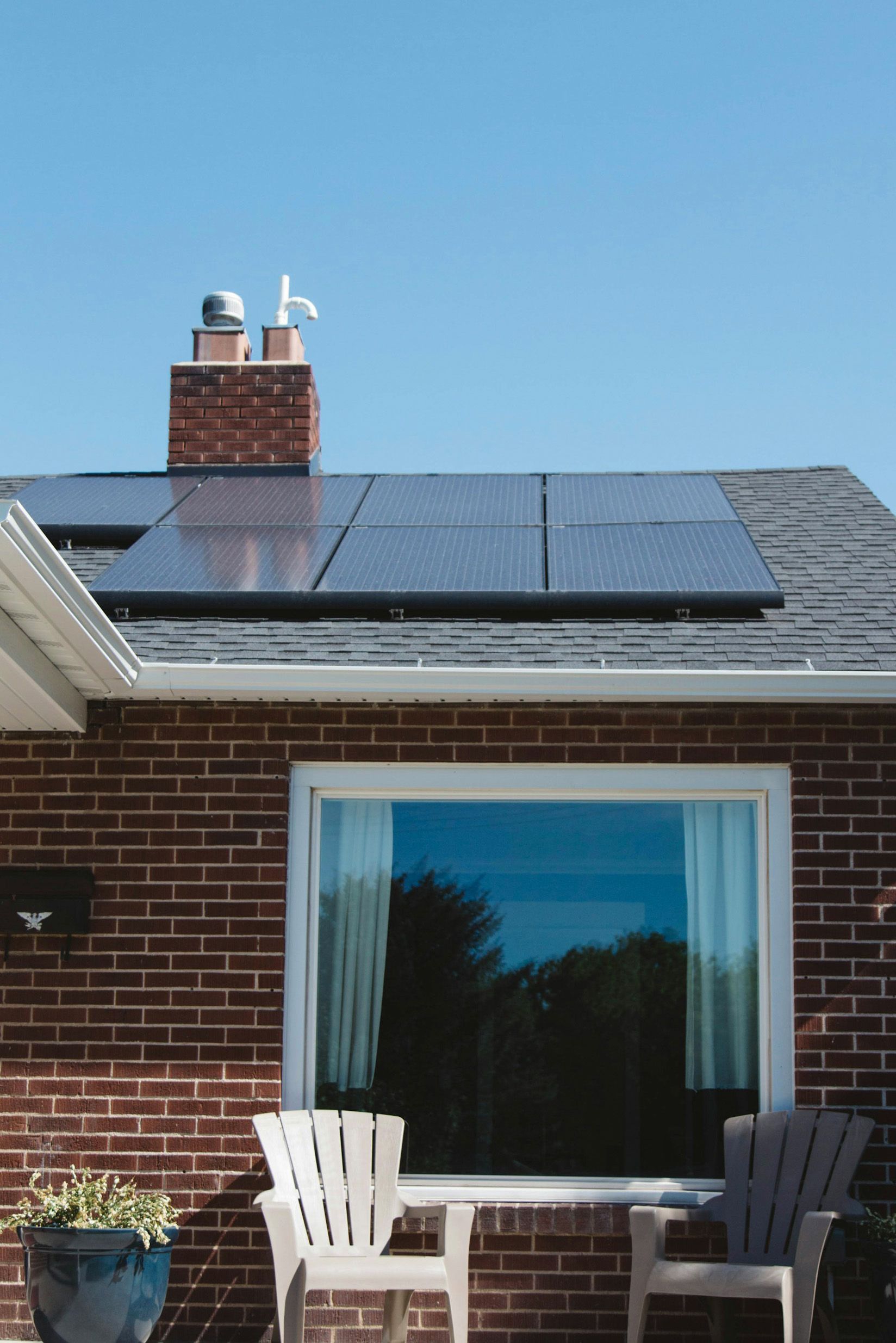 Residential house rooftop with solar panels under a clear blue sky.