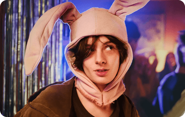 A young person in a pink bunny hat looks curiously at a party.
