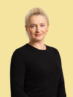 Blonde woman with her hair pulled back, wearing a black crewneck shirt against a yellow background.