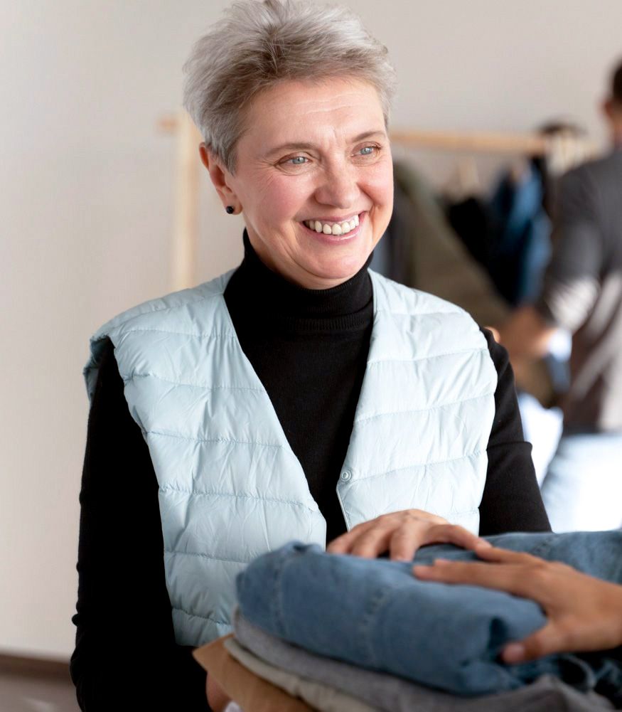 Smiling older woman in a blue vest exchanges folded blue clothes with another person.
