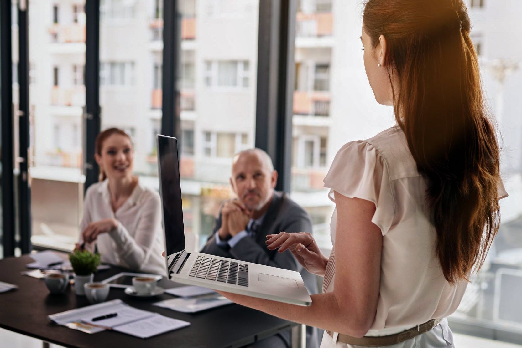 Woman presenting to colleagues with a laptop in a modern conference room.