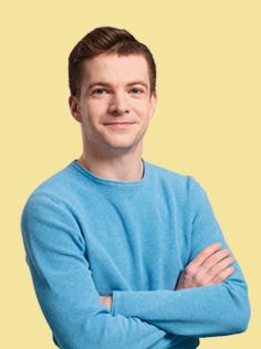 A young man with short brown hair wears a light blue sweater.