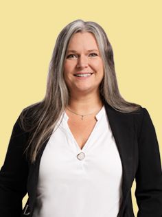 A woman with long gray hair, glasses, and a black jacket smiles.