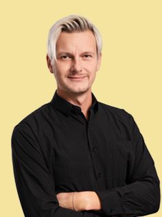 A man with graying hair, wearing a black collared shirt, smiles.
