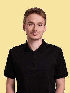 A man with short dark hair and a collarless black shirt smiles.