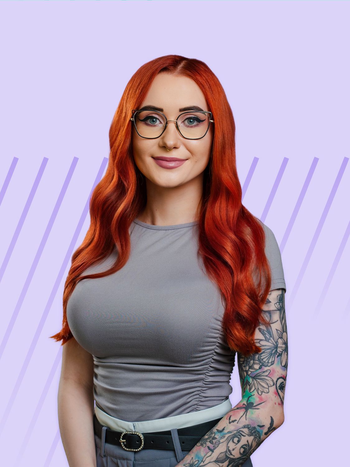 A smiling woman with long red hair and glasses, wearing a grey shirt and tattoos.