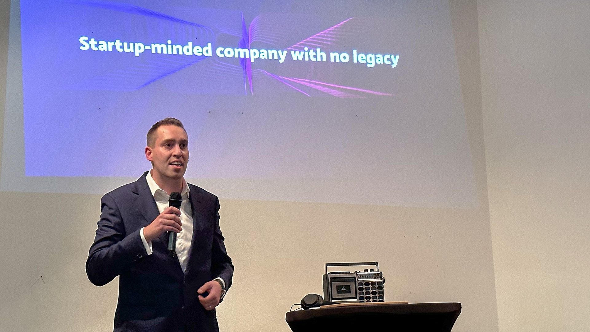 Man in suit speaking at a presentation with "Startup-minded company" on screen.