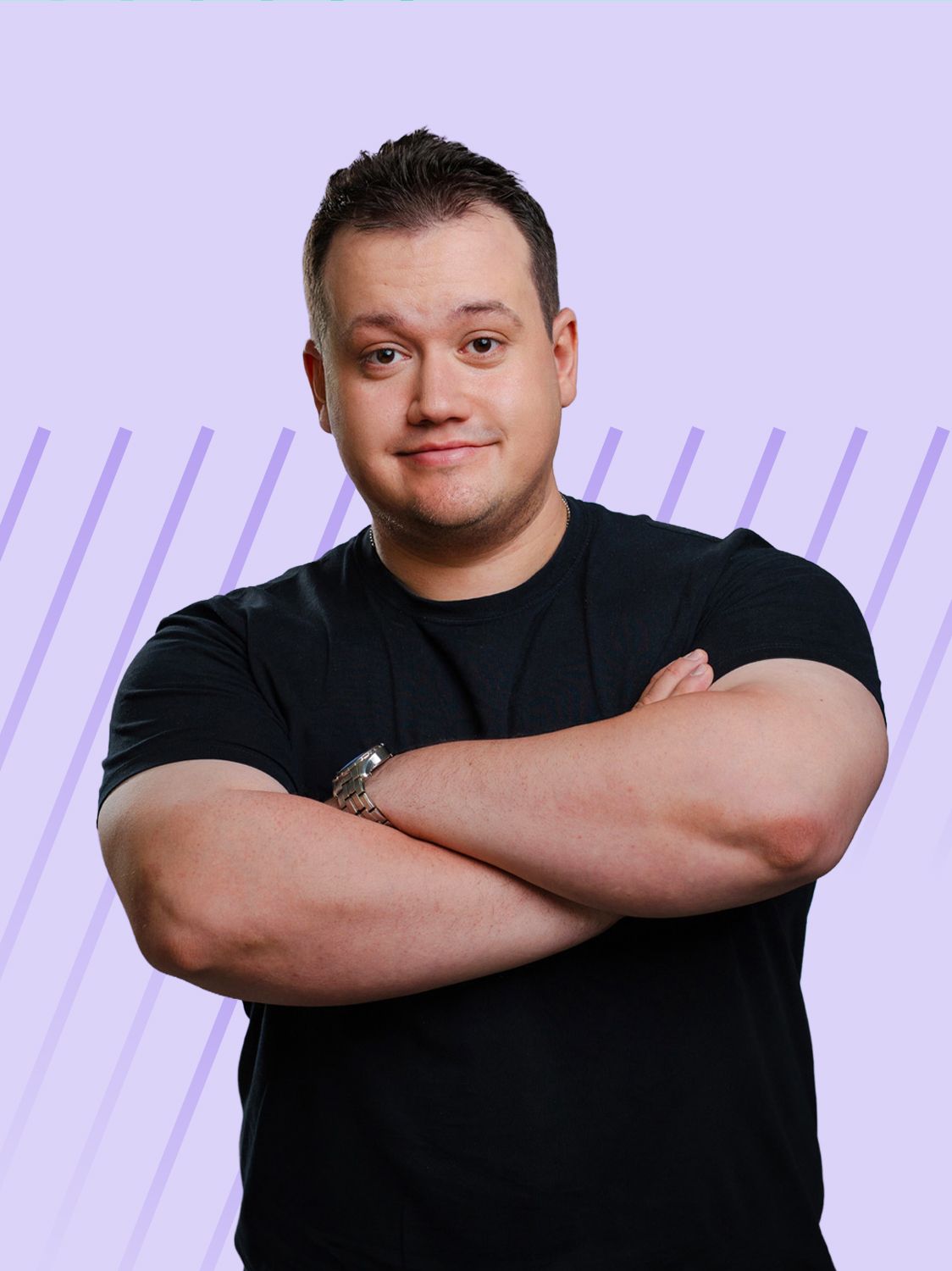 Man with dark hair and black t-shirt standing with arms crossed, smiling slightly.